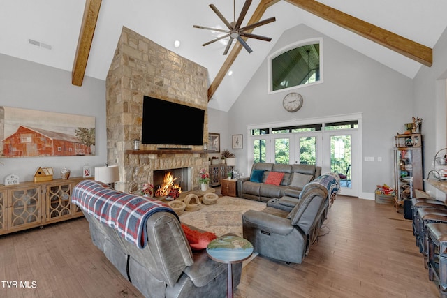 living room featuring visible vents, beam ceiling, a stone fireplace, and wood finished floors