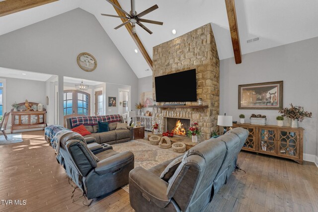 living room featuring beamed ceiling, high vaulted ceiling, hardwood / wood-style floors, ceiling fan, and a stone fireplace