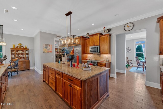 kitchen with appliances with stainless steel finishes, dark wood-type flooring, decorative light fixtures, and a center island with sink