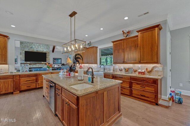 kitchen featuring a center island with sink, a stone fireplace, sink, a chandelier, and light wood-type flooring