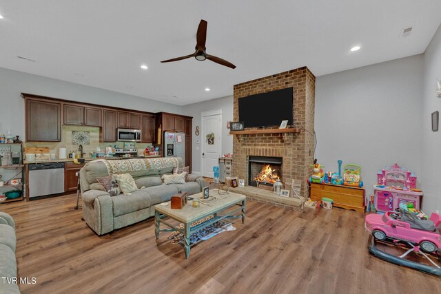 living room with light wood-type flooring, a brick fireplace, and ceiling fan