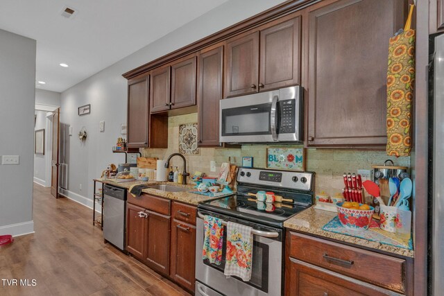 kitchen featuring appliances with stainless steel finishes, dark hardwood / wood-style flooring, light stone counters, and sink