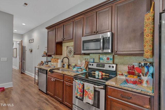 kitchen featuring backsplash, light stone countertops, wood finished floors, stainless steel appliances, and a sink