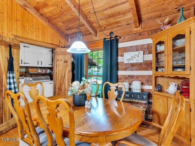 dining room with light hardwood / wood-style floors, wooden walls, washing machine and clothes dryer, and vaulted ceiling with beams