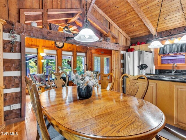 dining space featuring light wood-type flooring, wood ceiling, wood walls, vaulted ceiling with beams, and french doors