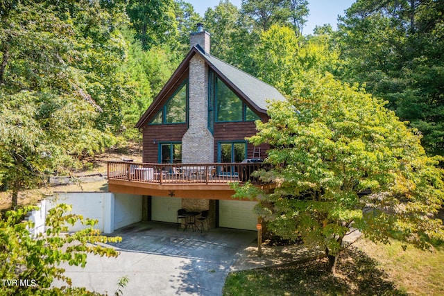 back of house with driveway, a garage, a chimney, and a wooden deck