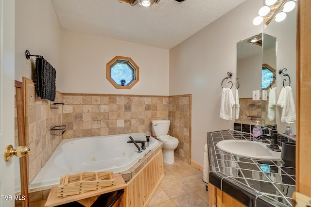 bathroom featuring vanity, tile patterned floors, a relaxing tiled tub, toilet, and a textured ceiling