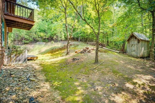 view of yard featuring an outbuilding, a forest view, a storage unit, and a wooden deck