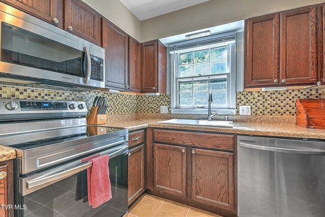 kitchen with appliances with stainless steel finishes, light tile patterned floors, decorative backsplash, and sink