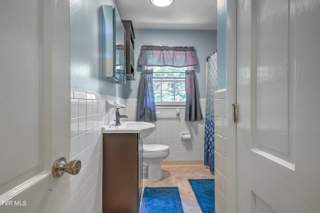 bathroom featuring a textured ceiling, vanity, tile walls, toilet, and tile patterned floors