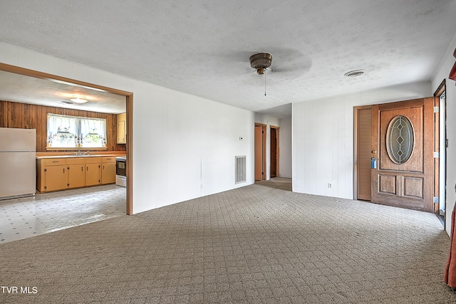 unfurnished living room featuring ceiling fan, light colored carpet, wooden walls, and a textured ceiling