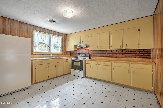 kitchen featuring white appliances, sink, wooden walls, and a textured ceiling