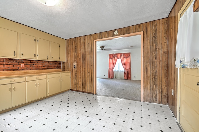 kitchen featuring light colored carpet, ceiling fan, wooden walls, and a textured ceiling