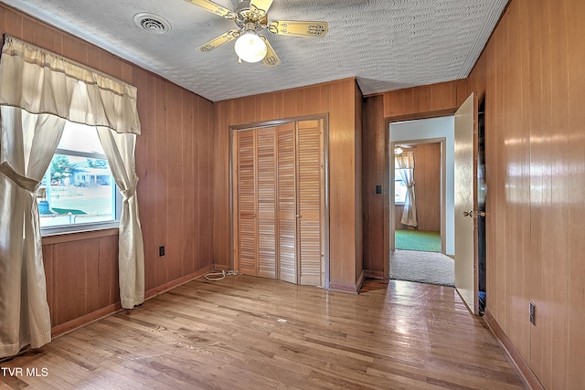 unfurnished bedroom with a closet, ceiling fan, wooden walls, and light hardwood / wood-style flooring