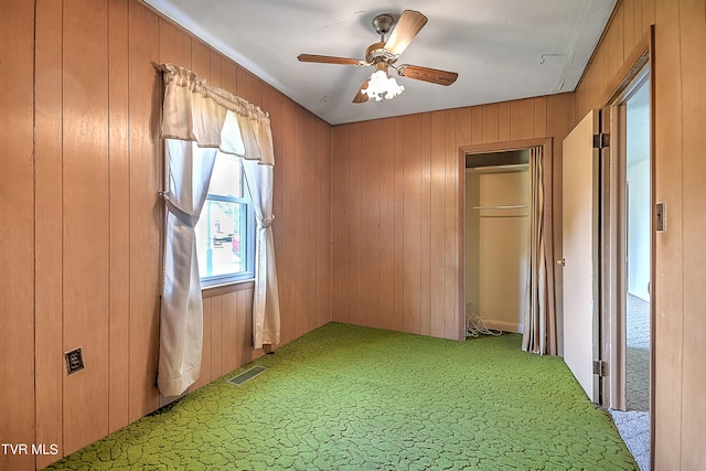 unfurnished bedroom with carpet flooring, a closet, ceiling fan, and wooden walls