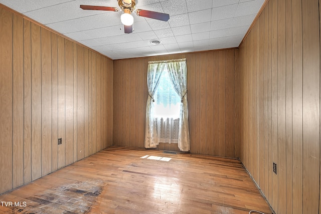 spare room with ceiling fan, wooden walls, and light hardwood / wood-style floors