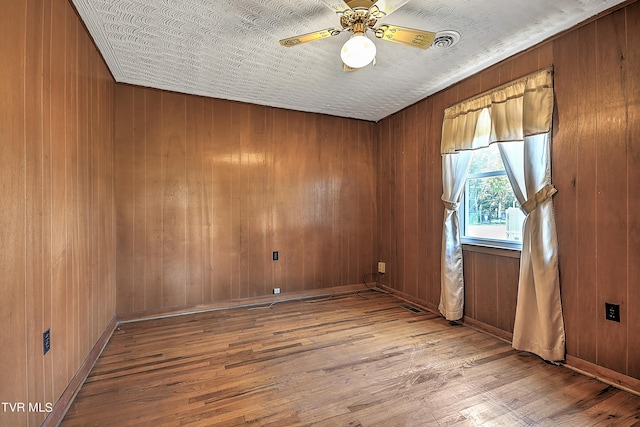 unfurnished room with a textured ceiling, light hardwood / wood-style flooring, ceiling fan, and wooden walls