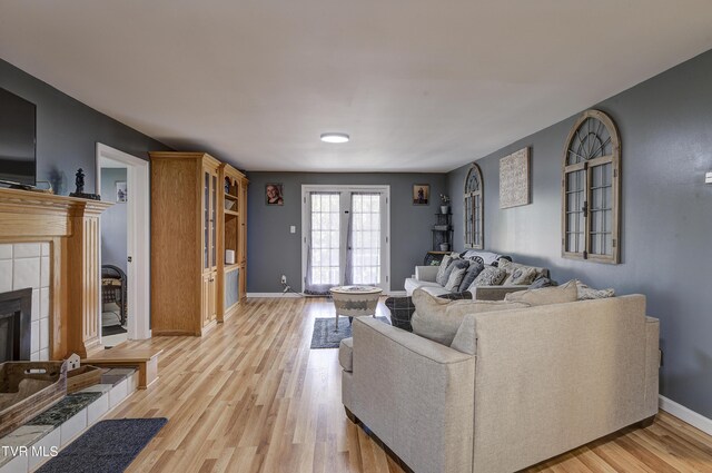 living room with a tiled fireplace, french doors, and light hardwood / wood-style floors