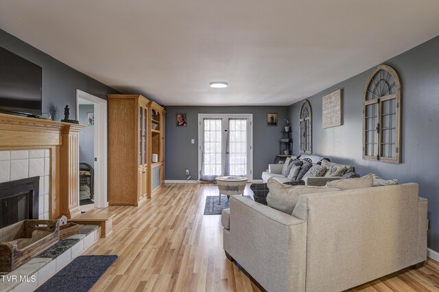 living room featuring light wood-type flooring, french doors, and a tile fireplace