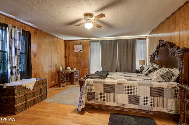 bedroom with crown molding, ceiling fan, wood walls, and light hardwood / wood-style floors