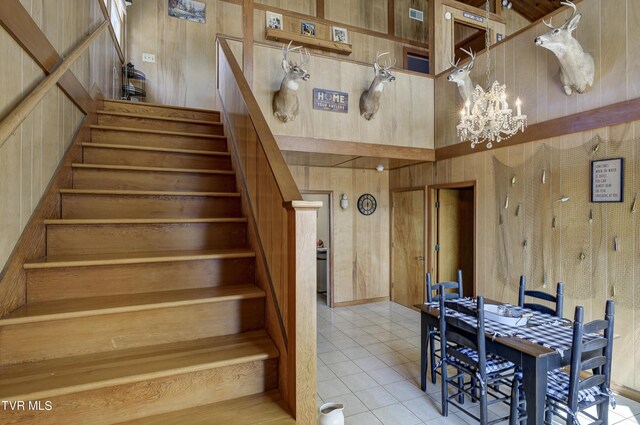 stairs featuring tile patterned flooring, wood walls, and a chandelier