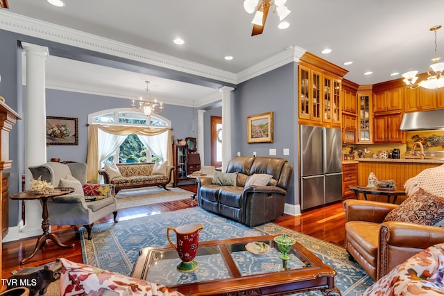 living room featuring ornamental molding, ceiling fan with notable chandelier, wood-type flooring, and ornate columns