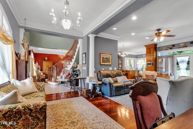 living room featuring ornamental molding, ceiling fan with notable chandelier, hardwood / wood-style flooring, and ornate columns