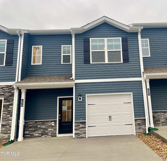 multi unit property with driveway, stone siding, a garage, and roof with shingles