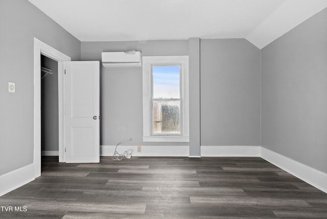 unfurnished bedroom featuring lofted ceiling, dark hardwood / wood-style floors, and a wall unit AC