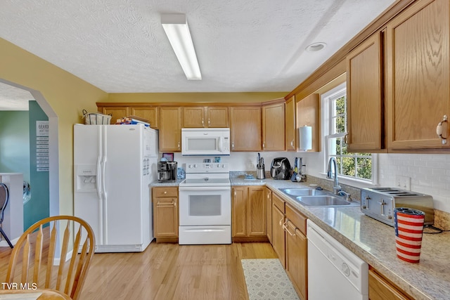 kitchen with a textured ceiling, white appliances, light hardwood / wood-style floors, sink, and light stone counters