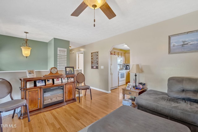 living room with light wood-type flooring, ceiling fan, and a textured ceiling