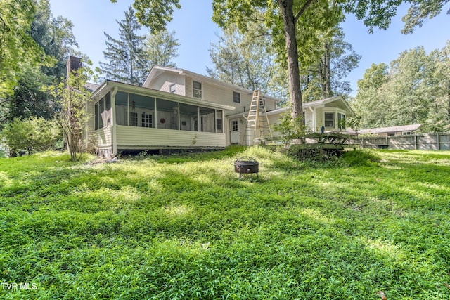 rear view of house with a fire pit, a sunroom, a chimney, a deck, and a yard