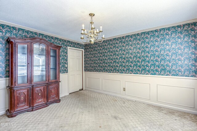 spare room featuring carpet flooring, ornamental molding, an inviting chandelier, and a textured ceiling