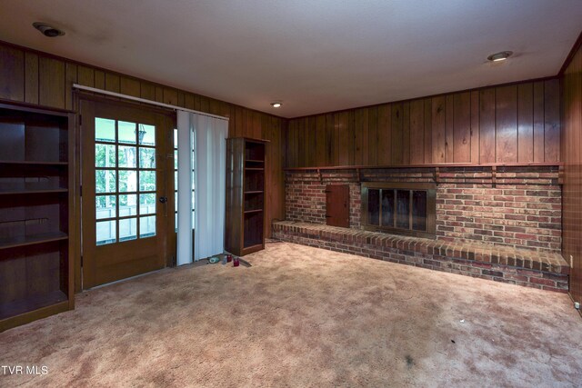 unfurnished living room featuring carpet, wood walls, and a brick fireplace