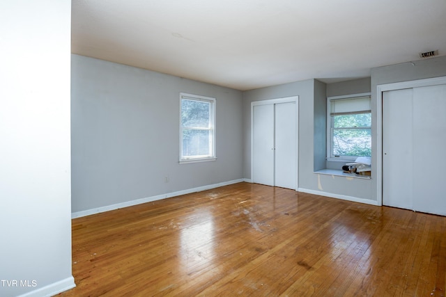 unfurnished bedroom featuring visible vents, two closets, baseboards, and wood-type flooring