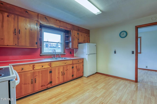 kitchen with freestanding refrigerator, stove, brown cabinets, a sink, and light wood finished floors