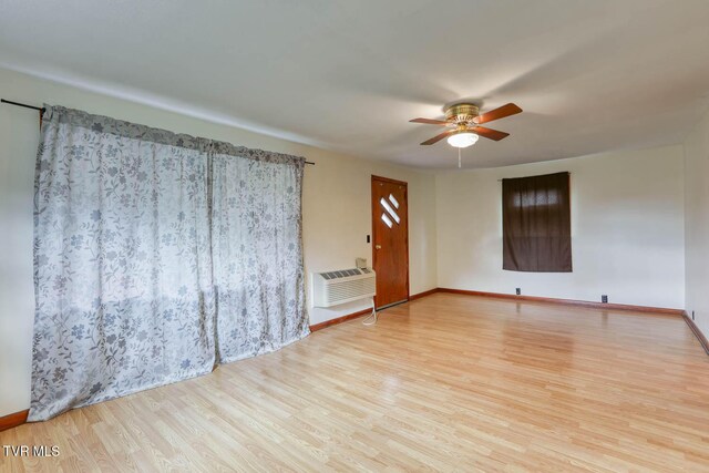 empty room with baseboards, a ceiling fan, wood finished floors, and an AC wall unit