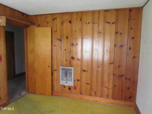 carpeted empty room with wood walls and heating unit