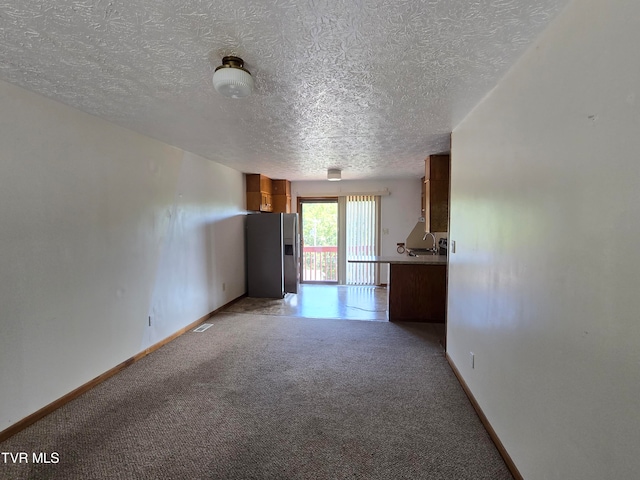 unfurnished living room with sink, light carpet, and a textured ceiling