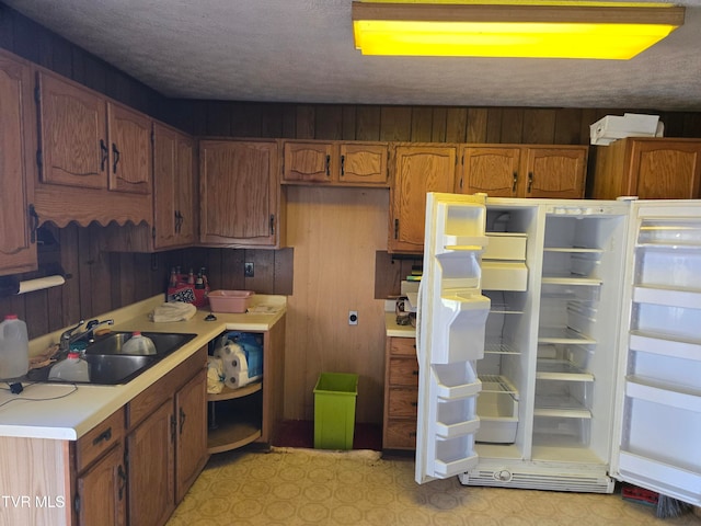 kitchen featuring wood walls, white fridge, sink, and a textured ceiling