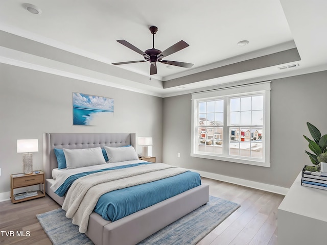 bedroom with a raised ceiling, ceiling fan, ornamental molding, and light wood-type flooring