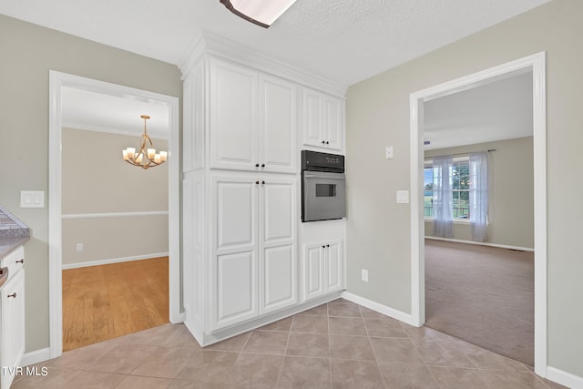 kitchen with white cabinetry, a textured ceiling, light tile patterned floors, oven, and an inviting chandelier