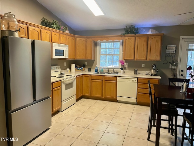 kitchen with white appliances, light tile patterned floors, vaulted ceiling, and sink