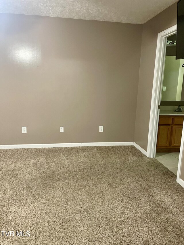 interior space featuring a textured ceiling, light colored carpet, and ensuite bath