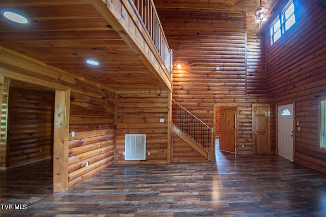 interior space with a towering ceiling, dark wood-type flooring, log walls, and wood ceiling