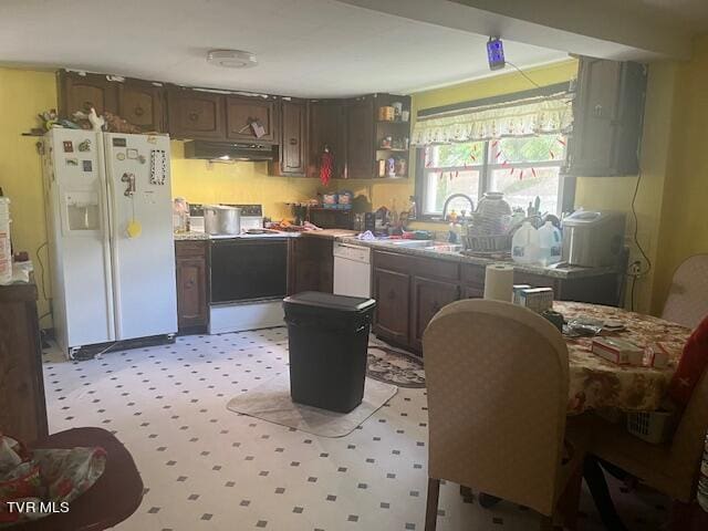 kitchen featuring white appliances, light floors, under cabinet range hood, and a sink