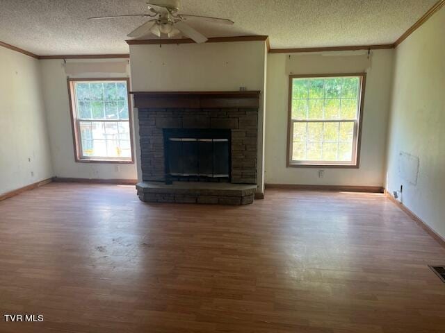 unfurnished living room with a wealth of natural light, a stone fireplace, crown molding, and wood finished floors