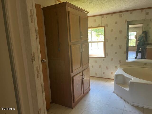 bathroom with wallpapered walls, plenty of natural light, a bath, and a textured ceiling