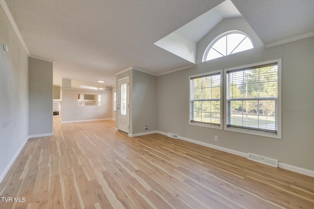 empty room with light wood-type flooring, vaulted ceiling, crown molding, and a textured ceiling