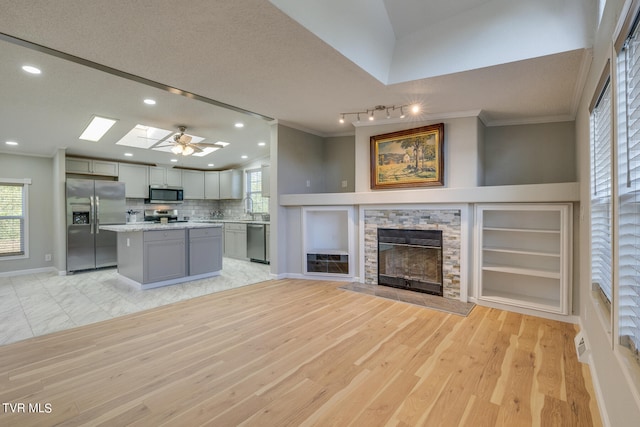 kitchen with gray cabinets, a fireplace, ceiling fan, appliances with stainless steel finishes, and light hardwood / wood-style floors